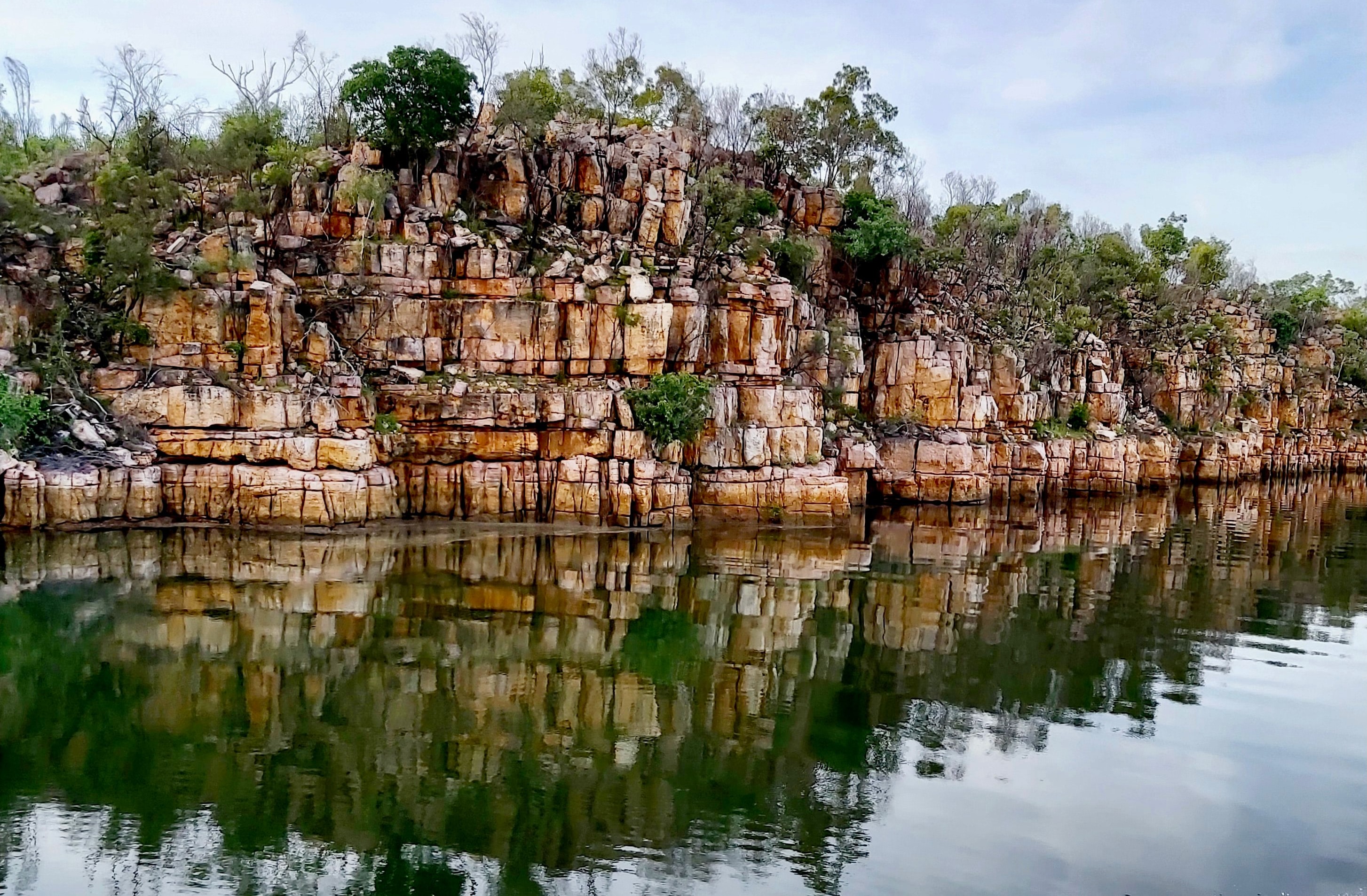 Photo of water reflecting the image of a stratified rock cliff
